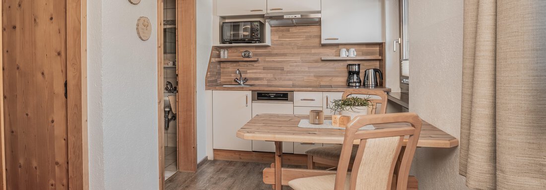 Eine moderne Küche mit Holzdetails und einem Esstisch. Der Raum ist hell und einladend, ideal für eine kleine Mahlzeit. - Appartements Alpenrose - Huben