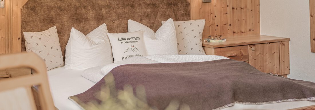 Ein gemütliches Schlafzimmer mit einem großen Bett und einer warmen Decke. Die Wände sind aus Holz, und die Einrichtung strahlt eine ruhige Atmosphäre aus. - Appartements Alpenrose - Huben