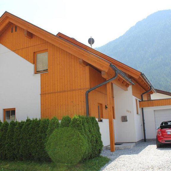 A modern house with wooden cladding and a garage space. In front of the house, there is a well-maintained hedge. - Chalet Mühle - Huben