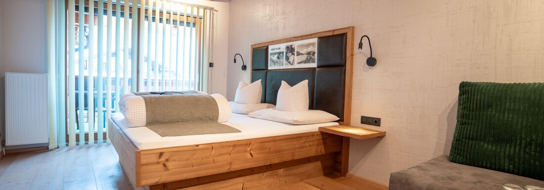 A modern room with a double bed and wooden floor.  
Large windows let in plenty of light and offer a view outside. - Genusshotel Alpenblick - Huben