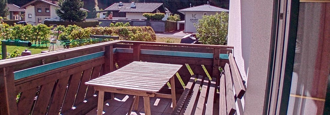 A sunny balcony with a wooden chair and a table. In the background, green meadows and mountains can be seen. - Haus Christoph im Herzen des Ötztals - Huben