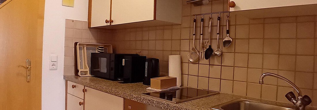 A modern kitchen with white cabinets and gray granite. There is a stove, a sink, and several appliances. - Haus Christoph im Herzen des Ötztals - Huben