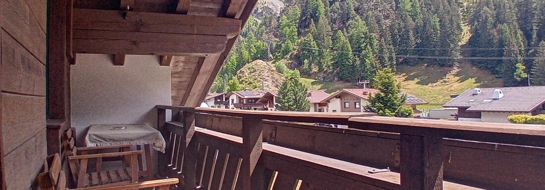A balcony with a wooden railing and two chairs. In the background, green mountains and a blue sky can be seen. - Haus Christoph im Herzen des Ötztals - Huben