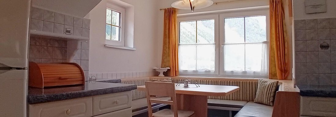 A bright kitchen with a table and chairs as well as a bench. Large windows let in plenty of light. - Haus Christoph im Herzen des Ötztals - Huben
