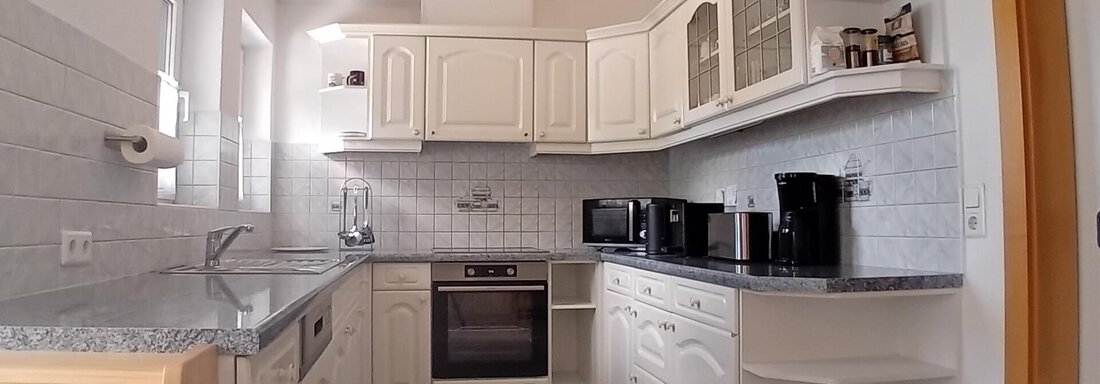 A modern kitchen with white cabinets and gray countertops. The equipment includes an oven, several coffee machines, and a cozy seating area. - Haus Christoph im Herzen des Ötztals - Huben