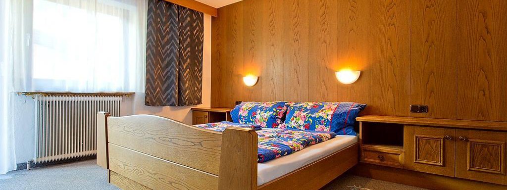 Ein gemütliches Schlafzimmer mit einem großen Bett und bunten Bettbezügen. Die Holzvertäfelung und der Teppich schaffen eine warme Atmosphäre. - Haus Max - Huben