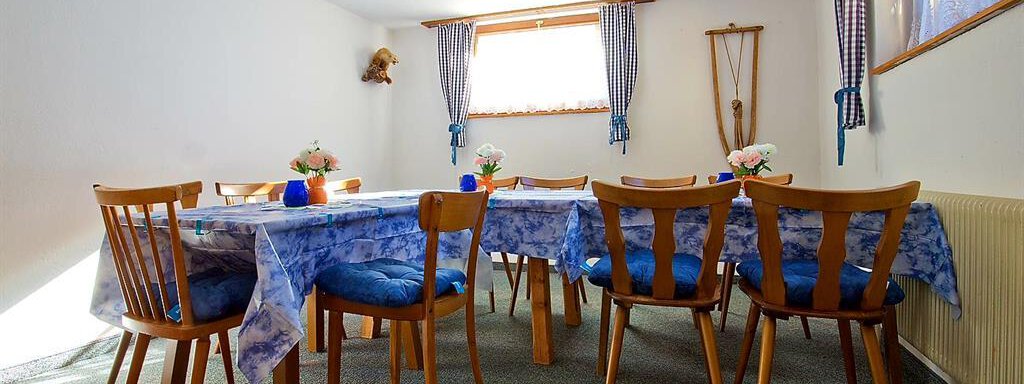 Ein einladender Essbereich mit einem langen Tisch und vielen Stühlen. Die Tische sind mit blauen Tischdecken und kleinen Blumendekorationen geschmückt. - Haus Max - Huben