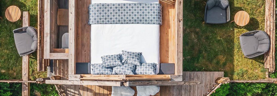 Ein gemütliches Baumhaus mit einem großen Bett und modernen Möbeln. Die Umgebung ist grün und einladend, ideal zum Entspannen. - Naturcamping Kuprian - Ötztal - Huben