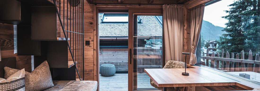 Ein gemütlicher Wohnraum mit Holzwänden und großen Fenstern. Der Raum hat einen Esstisch und eine Aussicht auf die umliegenden Berge. - Naturcamping Kuprian - Ötztal - Huben