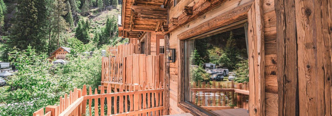 Eine Holzterrasse mit Blick auf eine grüne Landschaft und Bäume. Das Häuschen vermittelt eine gemütliche, alpine Atmosphäre. - Naturcamping Kuprian - Ötztal - Huben