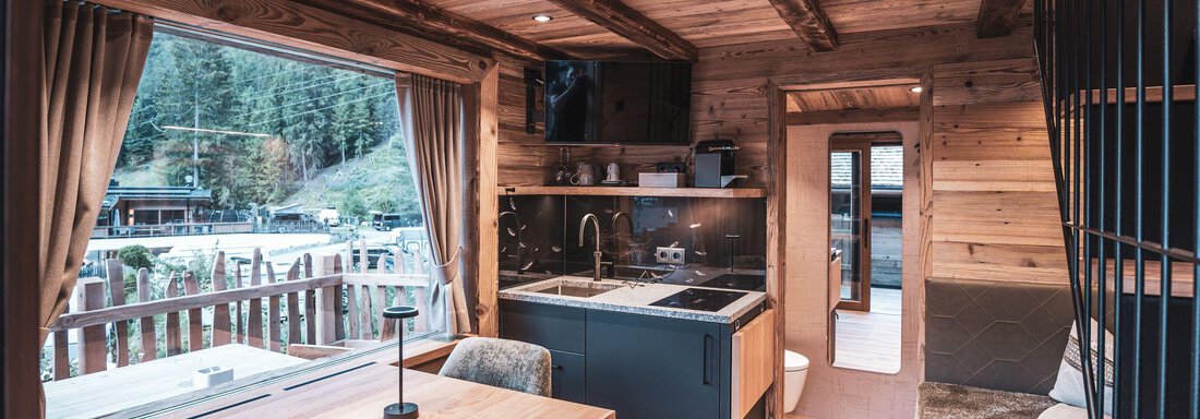 Eine gemütliche Holzwohnung mit einer modernen Küche und einem Essbereich. Große Fenster bieten einen schönen Blick auf die Natur draußen. - Naturcamping Kuprian - Ötztal - Huben