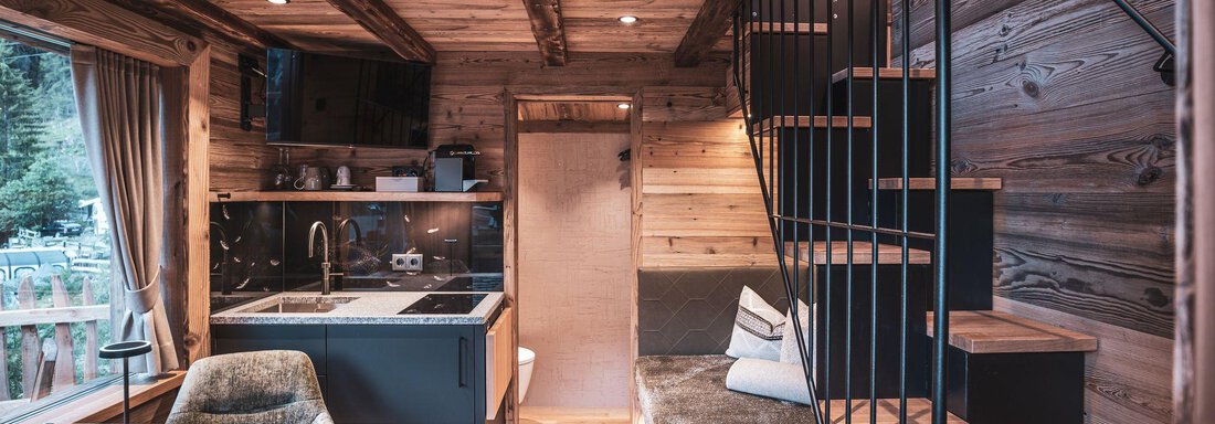 Ein gemütliches Holzinnendesign mit einer offenen Küche und einem Esstisch. Die Treppe führt zu einer höheren Ebene, umgeben von warmen Holztönen. - Naturcamping Kuprian - Ötztal - Huben