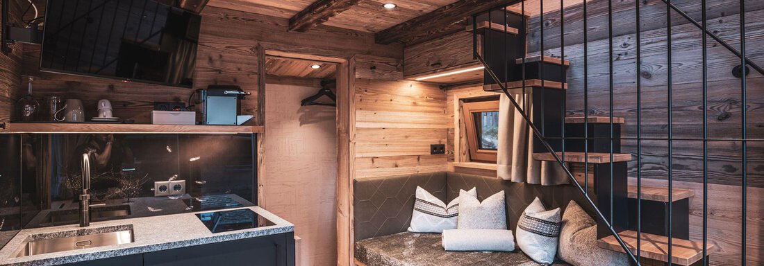 Eine gemütliche Inneneinrichtung mit Holzdetails und einem modernen Küchenelement. Eine Wendeltreppe führt zu einem oberen Bereich, der einladend wirkt. - Naturcamping Kuprian - Ötztal - Huben
