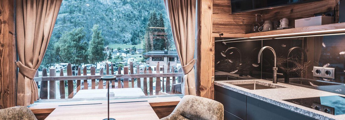 Eine moderne Küche mit einem Holztisch und bequemen Stühlen. Große Fenster bieten einen Blick auf die Berge und die Natur. - Naturcamping Kuprian - Ötztal - Huben