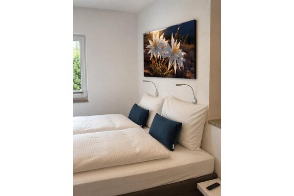 Doppelbett im ONO Apartment 1.1 A cozy bedroom with a double bed and pillows. A picture of flowers hangs on the wall. - ONO Apartments - Huben