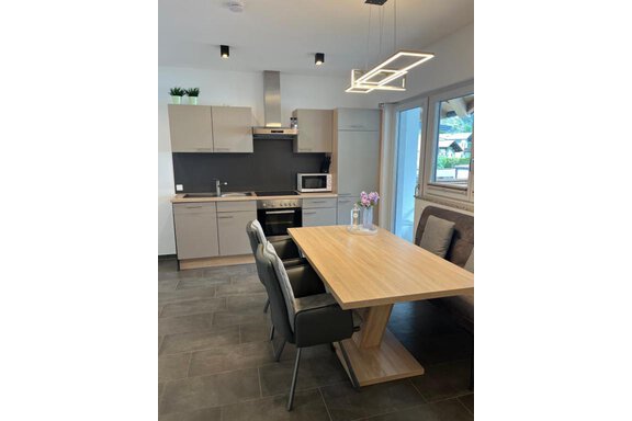 Moderne Küche mit hellen Möbeln und einem gemütlichen Essbereich. Ein Tisch aus Holz steht im Mittelpunkt, umgeben von eleganten Stühlen. - ONO Apartments - Huben