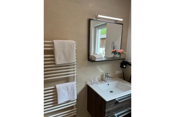 Ein modernes Bad mit einem Waschbecken, einem Spiegel und einem Handtuchhalter. Auf der Ablage stehen Blumen und zwei Gläser. - ONO Apartments - Huben