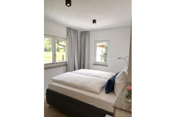 Ein modernes Schlafzimmer mit einem gemütlichen Doppelbett und hellen Vorhängen. Die Fenster bieten einen Blick auf die grüne Umgebung. - ONO Apartments - Huben