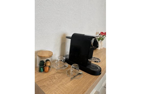 Eine moderne Kaffeemaschine steht auf einem Holztisch. Daneben befinden sich Kaffeekapseln und zwei Gläser. - ONO Apartments - Huben