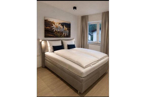 Doppelzimmer im ONO Apartment 2 A modern bedroom with a large, comfortable bed and two pillows. A picture of white flowers hangs on the wall. - ONO Apartments - Huben