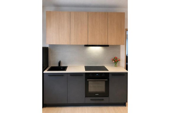Eine moderne Küche mit Holzoberflächen und einer glatten Arbeitsplatte. Der Herd und die Spüle sind in Schwarz gehalten, mit einer kleinen Blumendekoration auf der Arbeitsplatte. - ONO Apartments - Huben