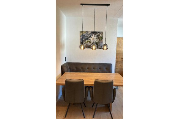 Ein modernes Esszimmer mit einer gemütlichen Bank und zwei Stühlen. Über dem Tisch hängen drei hängende Leuchten. - ONO Apartments - Huben