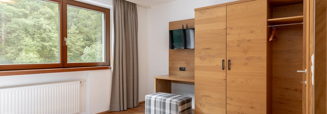 Ein einfaches Zimmer mit Holzfußboden, einem Fenster und einem Tisch. Es gibt eine Kommode, einen Fernseher und einen Hocker. - Alpenappartement Central Valley Penthouse - Längenfeld