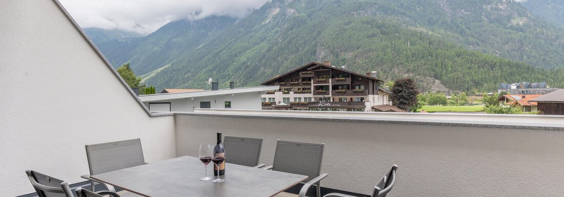 Eine gemütliche Terrasse mit einem Tisch und Stühlen. Im Hintergrund sind beeindruckende Berge und eine wolkige Himmel zu sehen. - Alpenappartement Central Valley Penthouse - Längenfeld