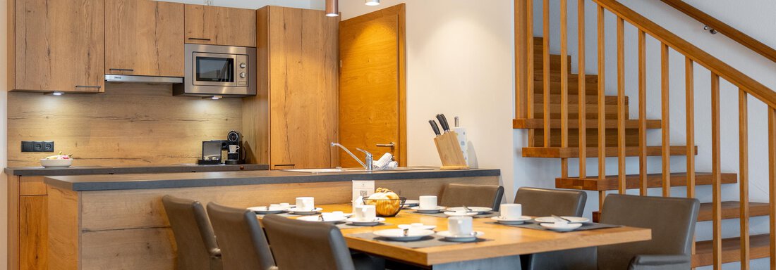 Eine moderne Küche mit einem Essbereich aus Holz und eleganten Stühlen. Die Treppe im Hintergrund bietet Zugang zu oberen Räumen. - Alpenappartement Central Valley Penthouse - Längenfeld