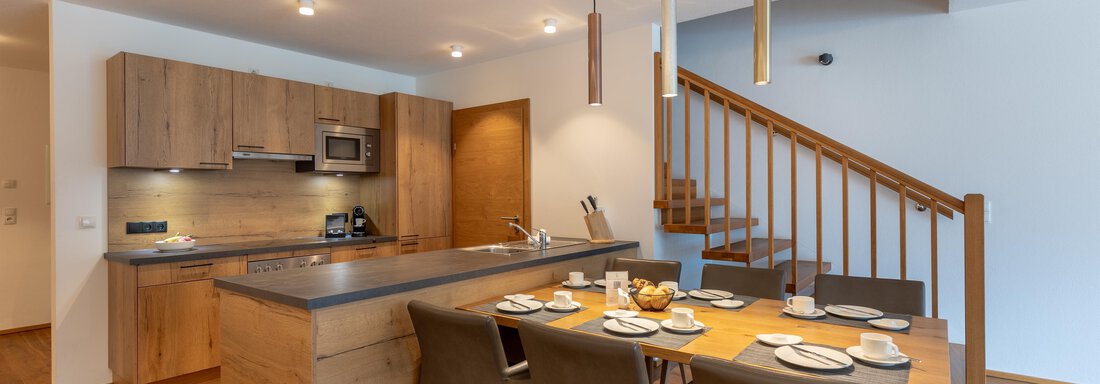 Eine moderne Küche mit Holzelementen und einer Essecke. Der Raum ist hell und einladend mit einer Treppe im Hintergrund. - Alpenappartement Central Valley Penthouse - Längenfeld