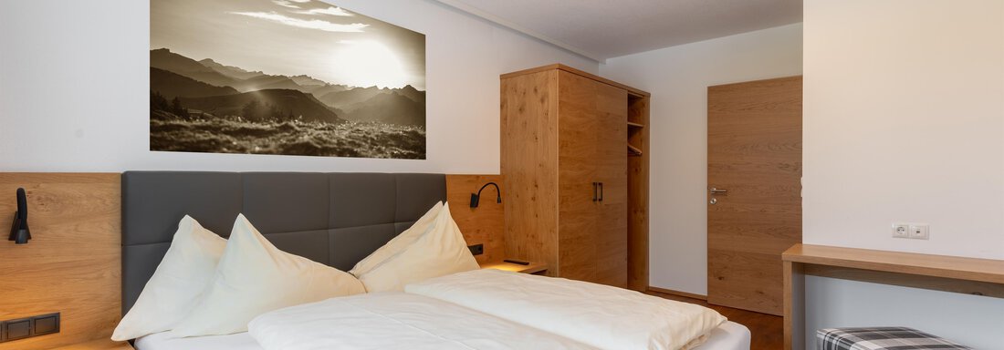 Ein modernes Schlafzimmer mit einem Doppelbett und Holzdekor. An der Wand hängt ein Landschaftsbild, und es gibt einen Kleiderschrank sowie eine kleine Sitzgelegenheit. - Alpenappartement Central Valley Penthouse - Längenfeld