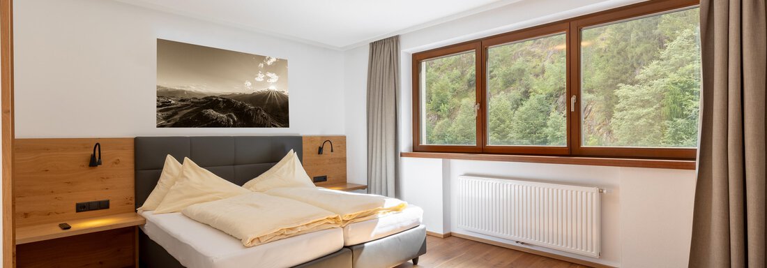 Ein modernes Schlafzimmer mit einem großen Fenster und Blick ins Grüne. Das Zimmer ist hell und minimalistisch eingerichtet. - Alpenappartement Central Valley Penthouse - Längenfeld
