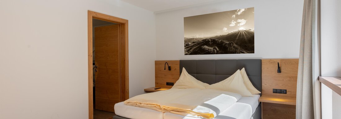 Ein modernes Schlafzimmer mit einem Doppelbett und Holzfußboden. An der Wand hängt ein Bild von Landschaften, und das Zimmer ist hell und freundlich. - Alpenappartement Central Valley Penthouse - Längenfeld