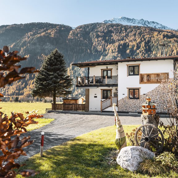 A charming residential house surrounded by picturesque nature and mountains. The property is well-maintained with beautiful landscaping and rustic details. - Alpenglühn Apart Längenfeld - Längenfeld