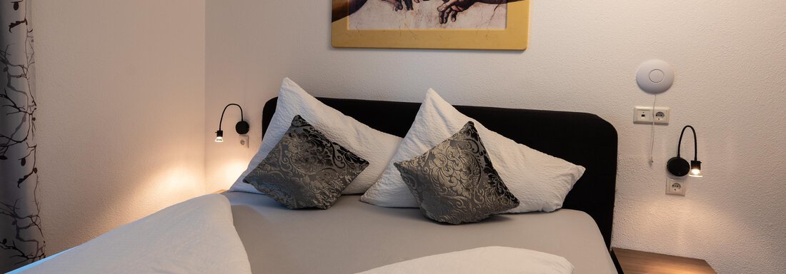 A cozy bedroom with a double bed and pillows. On the wall hangs a piece of art featuring two hands. - Apart Conny - Längenfeld