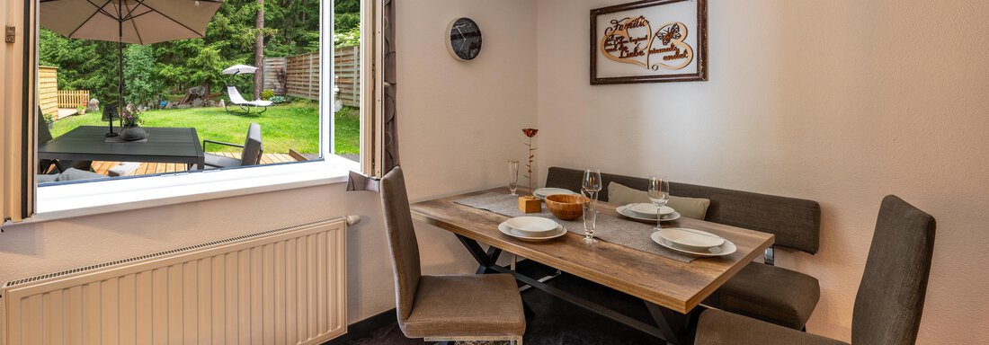 A cozy dining area with a table and chairs. Through the open window, a view of the garden can be seen. - Apart Conny - Längenfeld