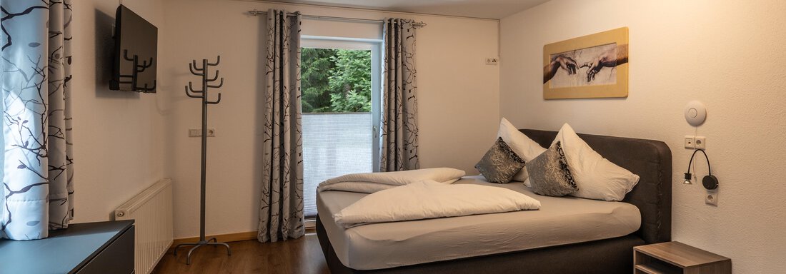 A modern bedroom with a double bed and large windows. The walls are bright and decorated with curtains and a piece of art. - Apart Conny - Längenfeld