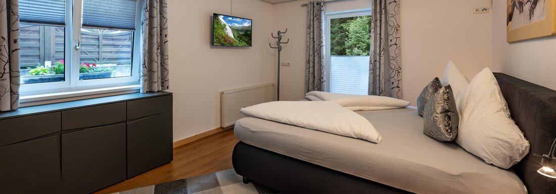 A modern bedroom with a comfortable bed and elegant decoration. The windows let in daylight and offer a view of the outdoors. - Apart Conny - Längenfeld
