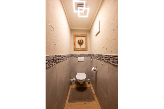A modern small restroom with gray tiles and a stylish wall mural. The room is brightly lit and feels inviting. - Apart Conny - Längenfeld