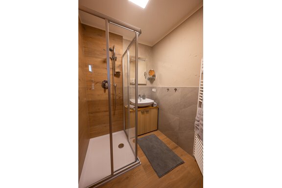 A modern bathroom with a glass shower and wooden details. The floor has a wood look, and the room feels bright and inviting. - Apart Conny - Längenfeld