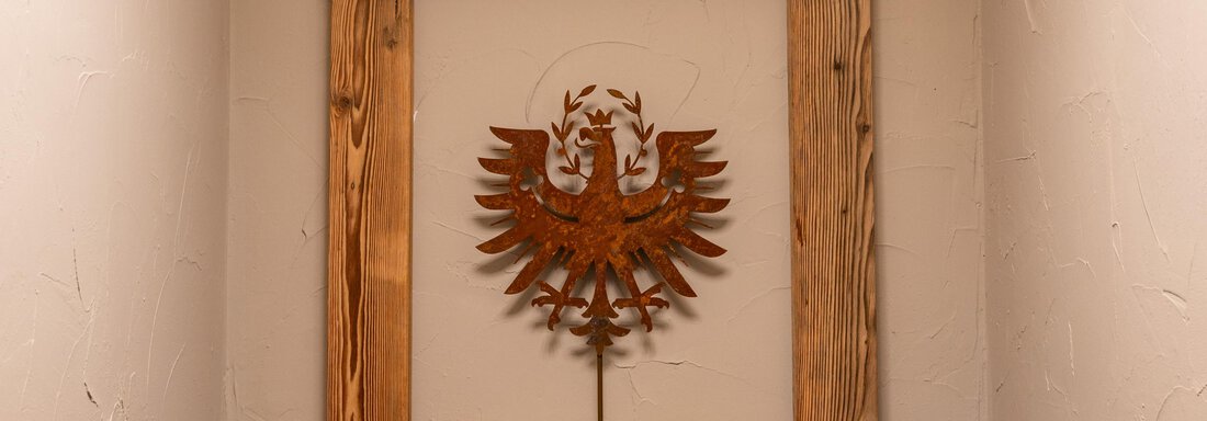 A wall decoration featuring a spread-winged eagle, framed by a rustic wooden frame. The wall is designed to be simple and elegant. - Apart Conny - Längenfeld