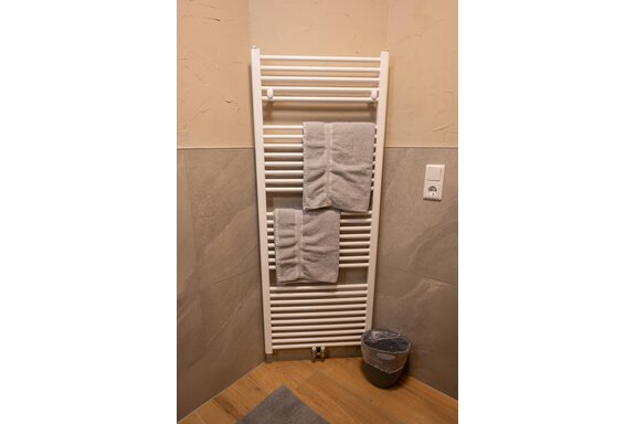 A white towel radiator with two gray towels. Next to the radiator stands a small trash can. - Apart Conny - Längenfeld