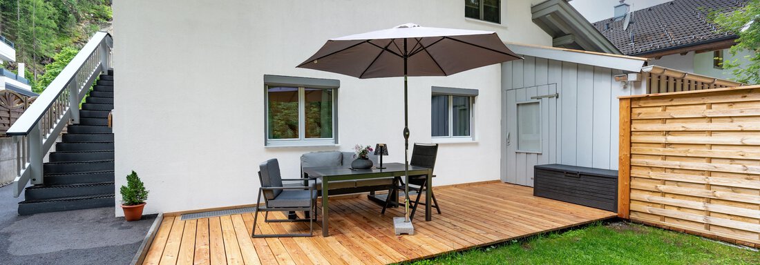 A terrace with a dining area and a sunshade. In the background, a white house and a green meadow can be seen. - Apart Conny - Längenfeld