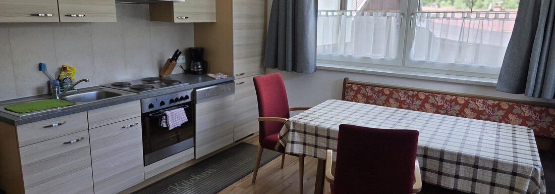 Eine helle Küche mit moderner Ausstattung und einem Esstisch. Neben dem Tisch steht ein roter Stuhl und das Fenster gibt viel Tageslicht. - Apart Luca - Längenfeld