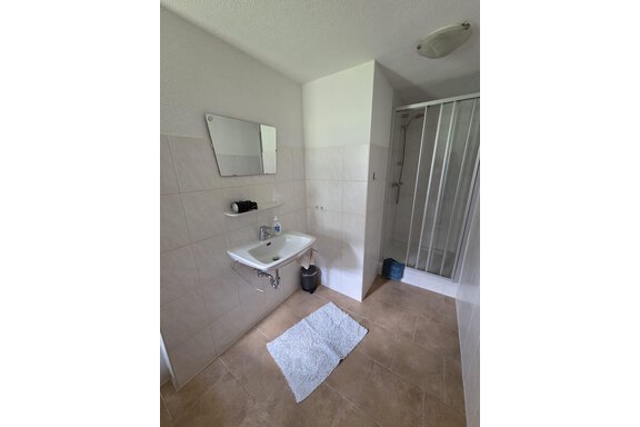 Ein modernes Badezimmer mit einem Waschbecken, einem Spiegel und einer Dusche. Der Boden ist gefliest und ein Handtuch liegt auf dem Boden. - Apart Luca - Längenfeld