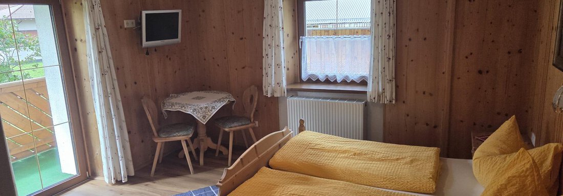 Ein gemütliches Schlafzimmer mit Holzvertäfelungen und zwei Einzelbetten. Ein kleiner Tisch mit Stühlen und ein Balkon sind ebenfalls zu sehen. - Apart Luca - Längenfeld