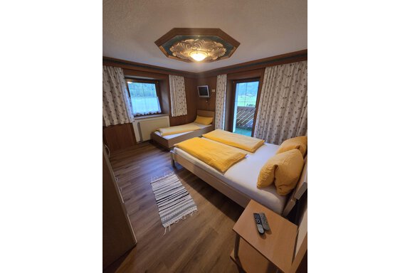 Ein gemütliches Zimmer mit einem Doppelbett und einem Einzelbett. Die Wände sind mit hellen Vorhängen geschmückt und der Raum ist gut beleuchtet. - Apart Luca - Längenfeld