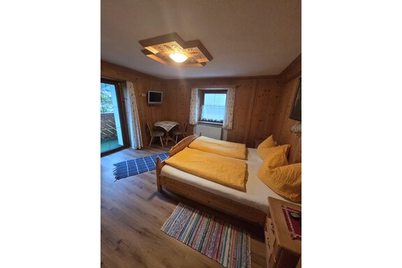 Ein gemütliches Zimmer mit zwei Betten und gelben Kissen. Der Raum hat Holzverkleidung und Zugang zu einem Balkon. - Apart Luca - Längenfeld