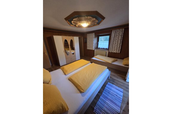 Ein gemütliches Schlafzimmer mit zwei Betten und gelben Bettdecken. Der Raum hat Holzverkleidung und ein Fenster mit Vorhängen. - Apart Luca - Längenfeld