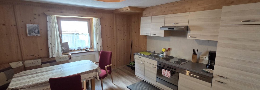 Eine moderne Küche mit Holzverkleidung und einem Esstisch. Das Zimmer ist hell und freundlich, mit einem Fenster, das Tageslicht hereinlässt. - Apart Luca - Längenfeld